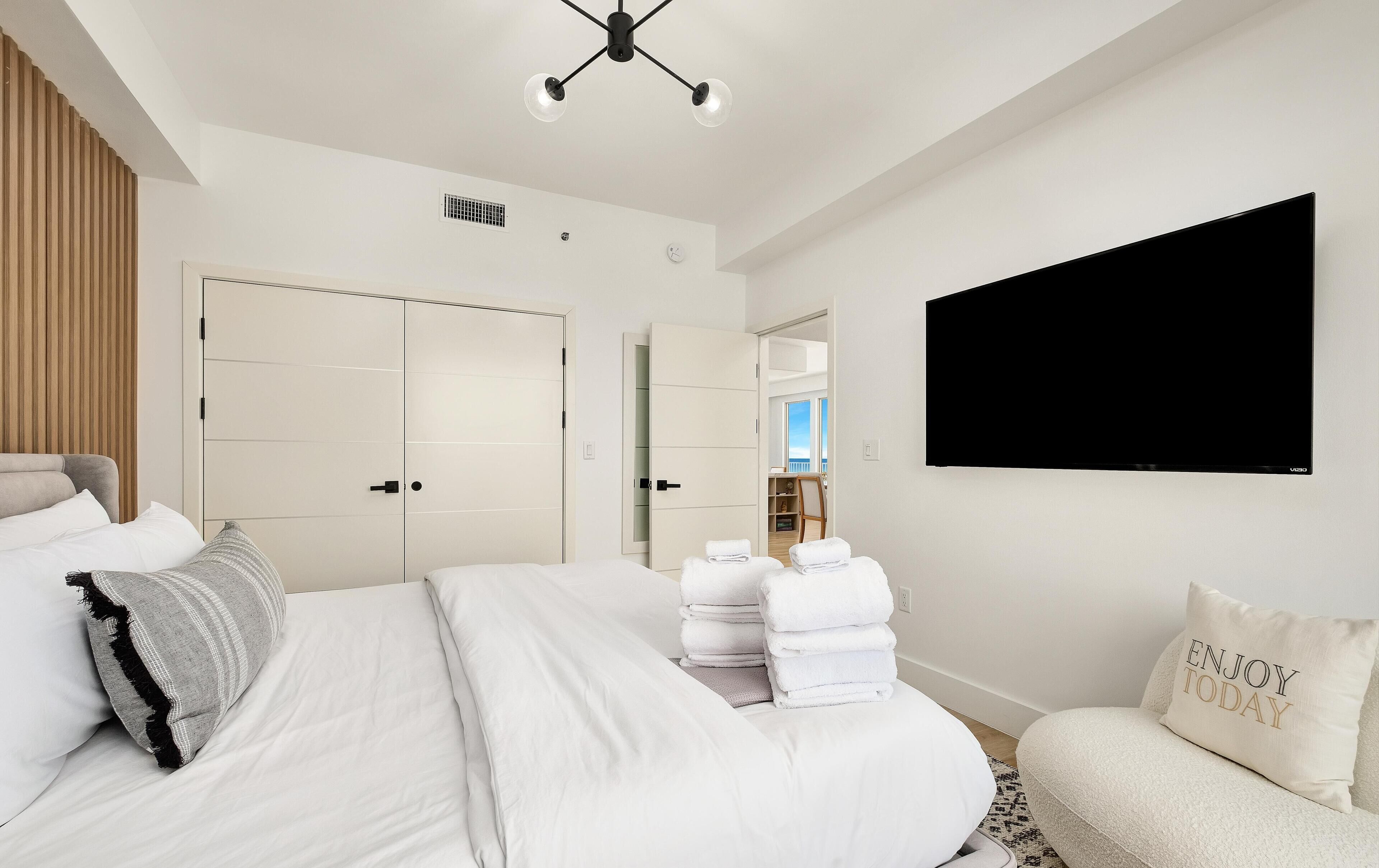 A modern hotel room with a large bed, a flat-screen TV, a wardrobe, and a view of the outdoors.