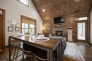 A rustic interior with a wooden dining table, bar stools, a fireplace, and a stone fireplace surround. - Lantern Hill, King Bed Suite, Hot Tub, Fire Pit (Broken)