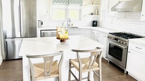 Una cocina moderna con armarios blancos, electrodomésticos de acero inoxidable, una isla central y dos sillas de mimbre.