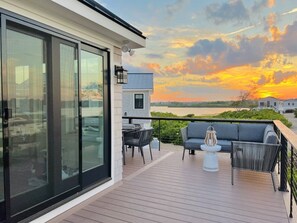 Una terraza moderna con sofá, sillas y mesa, con vistas a un cuerpo de agua al atardecer.