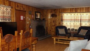 Et værelse med træpaneler, en pejs, et fjernsyn, en sofa og et spisebord med stole.