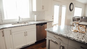 Une cuisine avec des meubles blancs, un plan de travail en granit, un lave-vaisselle et une horloge au mur.
