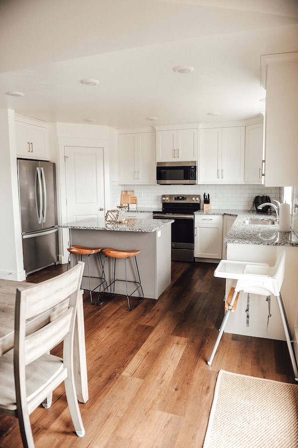 Enjoy cooking in this well-equipped kitchen with a refrigerator, oven, and microwave, complemented by a granite countertop and white cabinetry.