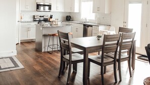Une cuisine moderne avec des meubles blancs, un îlot central et un coin repas doté de chaises en bois.