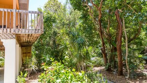 Un balcón de madera con vistas a un jardín exuberante y diverso, con árboles y plantas.