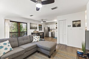 A modern living room with a sectional sofa, a ceiling fan, and a view of the kitchen and dining area. - The Florida Keys Treehouse in Marathon, FL (Marathon)