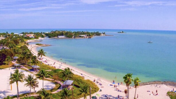 Un resort en la playa con una costa arenosa, palmeras y aguas azul turquesa.