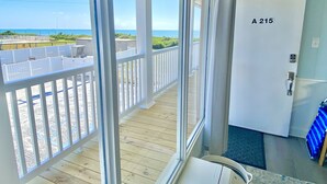 Un balcón con vistas a la playa y al océano, una puerta con la etiqueta “A 215”, y una ventana con vista a la playa.