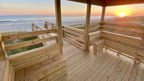 Una terraza de madera con bancos que da a una playa al atardecer.