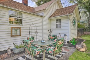 Ein Haus mit einer Terrasse, auf der sich ein Glastisch und Blumenschalen sowie ein Vogelhaus und ein Garten mit einer grünen Pflanze und Steinen befinden.