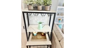 A white shelf unit with a black metal frame, holding a variety of items including a watering can, a tray with sticks, and a small plant. - Navarre Beach Front Whole House Large Yard. Kayaks + Paddle Boards Included.  (Navarre)