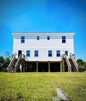 A two-story white building with a flat roof, a central entrance, and a covered front porch with stairs leading up to it. - Navarre Beach Front Whole House Large Yard. Kayaks + Paddle Boards Included. (Navarre)