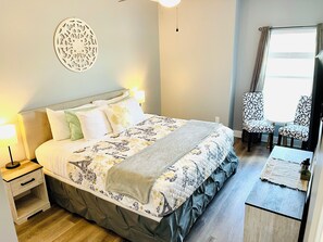 A neatly arranged bedroom with a bed, bedside table, lamp, decorative wall piece, and a window with curtains. - Navarre Beach Front Whole House Large Yard. Kayaks + Paddle Boards Included. (Navarre)