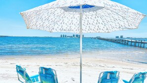 A beach with two blue and green striped beach chairs and a white umbrella with a pattern. - Navarre Beach Front Whole House Large Yard. Kayaks + Paddle Boards Included.  (Navarre)