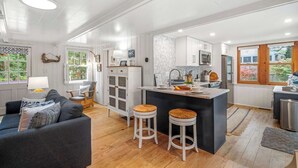 Une cuisine moderne avec des meubles blancs, un îlot central et un coin repas comprenant un canapé gris et deux tabourets.