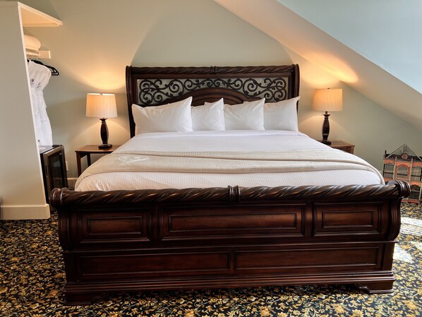 A large, dark wooden bed with a decorative headboard, white linens, two bedside lamps, and a patterned carpet. - Woodstone Manor Inc. (Galiano)