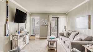 Een woonkamer met een bank, een salontafel, een aan de muur bevestigde televisie en een deur naar een balkon.