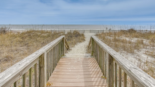 Een houten looppad dat naar een strand leidt, met een heldere lucht.