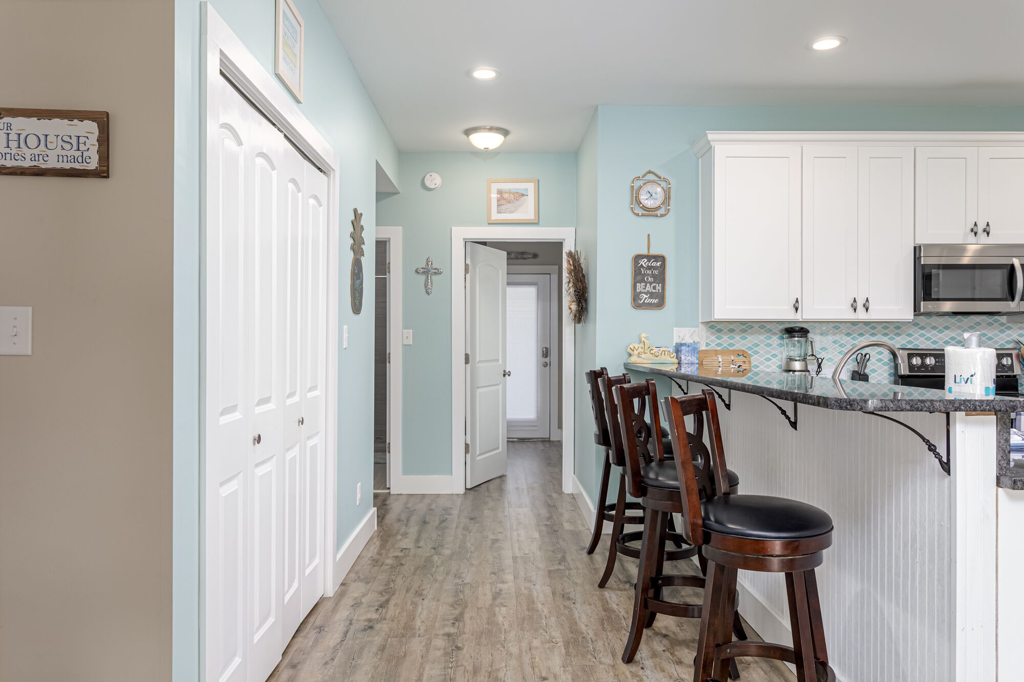 A kitchen with white cabinets, a microwave, and a bar area with stools.