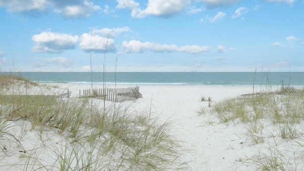 Une plage avec des dunes de sable et une clôture en bois.