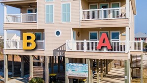 Une propriété située en bord de mer, comprenant un bâtiment à deux étages, des balcons et un passage piétonnier donnant accès à la plage.