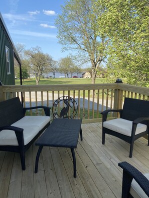 A wooden deck with two wicker chairs and a small table, overlooking a grassy area with trees and a body of water. - New lake view rental on Wolfcreek with boat ramp and lake access across the road (Grove)