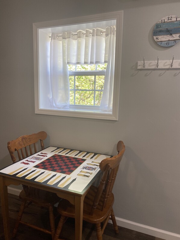 A dining table with a checkered tablecloth, two wooden chairs, a window with sheer curtains, and a wall-mounted clock. - New lake view rental on Wolfcreek with boat ramp and lake access across the road (Grove)