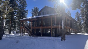 Una cabaña de madera con un porche cubierto y una escalera que lleva a la entrada, rodeada de árboles nevados.