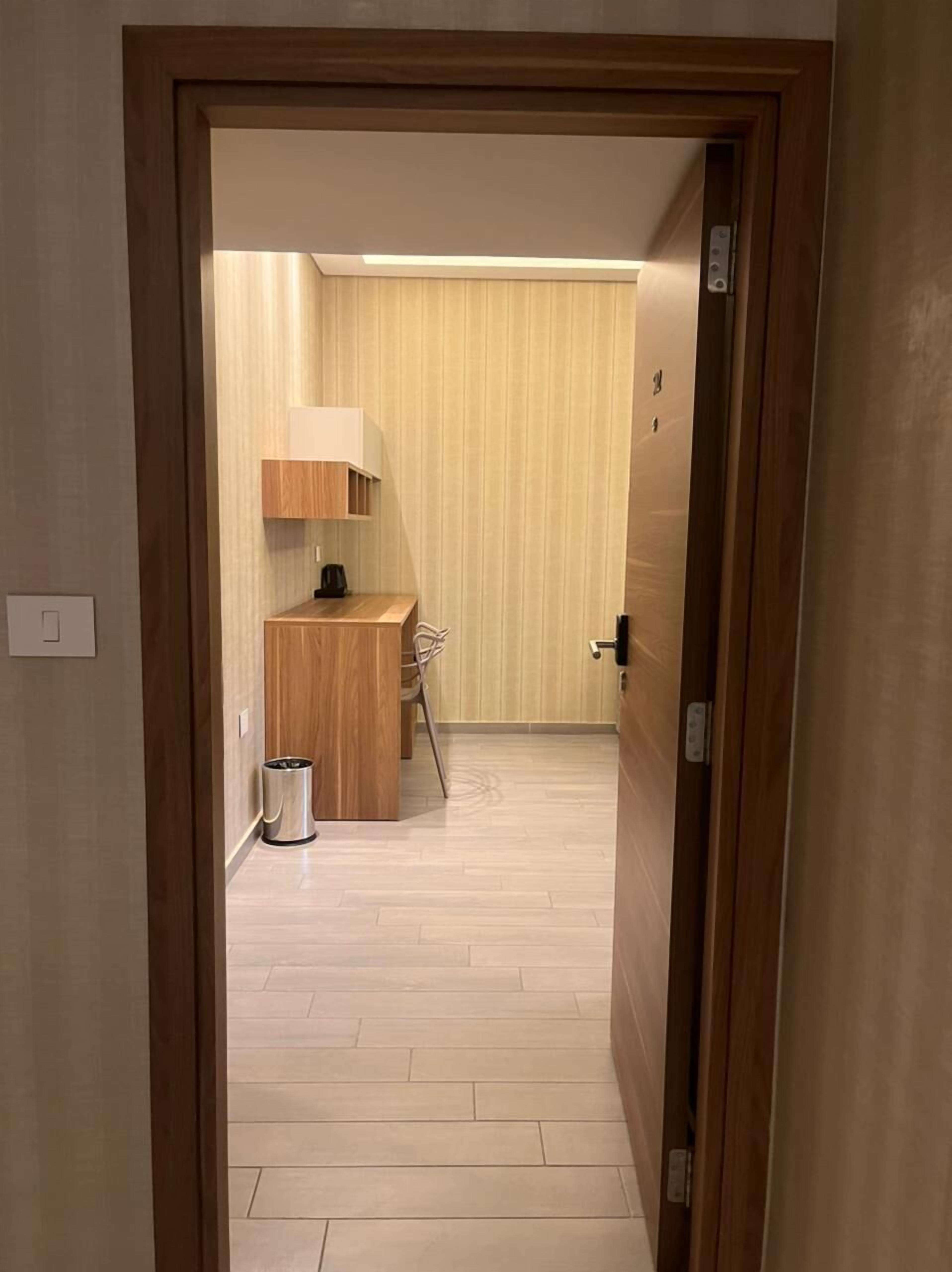 A hallway leading to a room with a wooden desk, chair, and a trash bin.