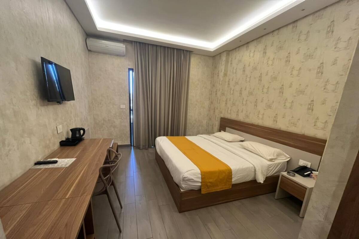 Habitación de hotel con un escritorio de madera, una cama con una manta amarilla, una mesita de noche y un televisor montado en la pared.