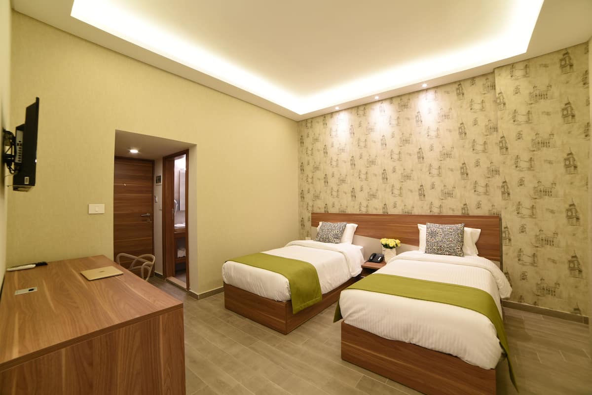 Habitación de hotel con dos camas, un escritorio y un baño visible a través de una puerta abierta.