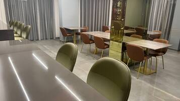 A modern dining area with multiple tables and chairs, a bar area with bottles, and large windows with curtains.