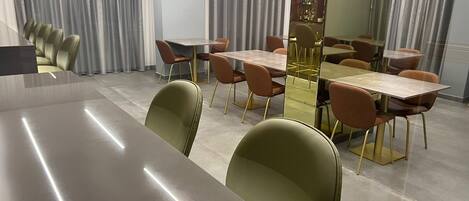 A modern dining area with multiple tables and chairs, a bar area with bottles, and large windows with curtains.