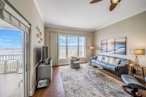 A living room with a large window, a sofa, a coffee table, and a ceiling fan.