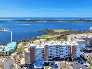 A high-rise hotel with multiple balconies, a swimming pool, and a view of a coastal area with water and greenery.