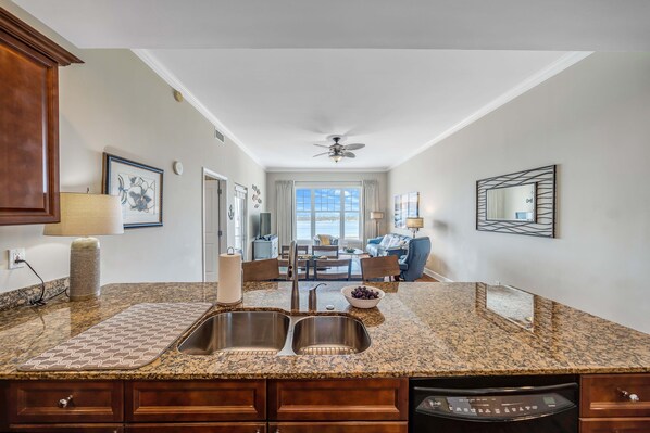 A kitchen with granite countertops, a double sink, and wooden cabinets. - FREE Daily Golf! Reflections 805 Amazing Top Floor View, Resort Pool, Hot Tub (Panama City Beach)