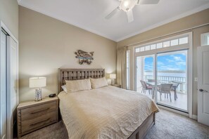 A bedroom with a large bed, a nightstand with a lamp, a ceiling fan, and a view of the outdoors through a sliding glass door.