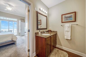 Une chambre à coucher avec un lit, une salle de bain avec un meuble-lavabo, un ventilateur de plafond et une grande fenêtre.