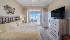 Une chambre à coucher avec un lit, une commode, une télévision et un balcon offrant une vue.