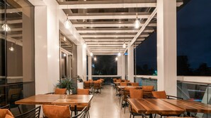 An outdoor dining area with wooden tables and chairs, large windows, and hanging pendant lights. - Maa Hotel and Suites (Nairobi)