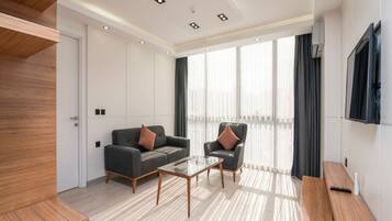 Una sala de estar moderna con un sofá, un sillón y una mesa de centro. Hay un televisor montado en la pared y una ventana con cortinas.