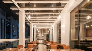 A modern restaurant interior with wooden tables and chairs, a central kitchen, and large windows. - Maa Hotel and Suites (Nairobi)