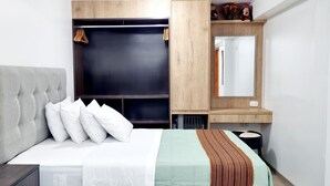 Une chambre d’hôtel avec un lit, une armoire, un miroir et une petite table.
