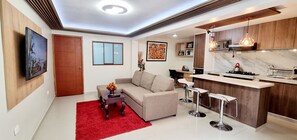 A modern living room with a sofa, a coffee table, and a red rug. There is a kitchen area with a bar and stools.
