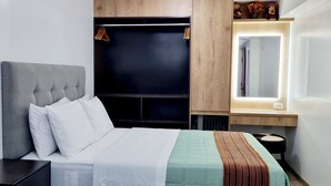 Une chambre à coucher moderne avec une tête de lit capitonnée, un grand lit avec une literie blanche, une tête de lit sombre, une armoire en bois et une table de chevet avec une lampe.