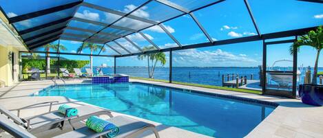 A pool area with clear blue water, lounge chairs, and a view of the sea.