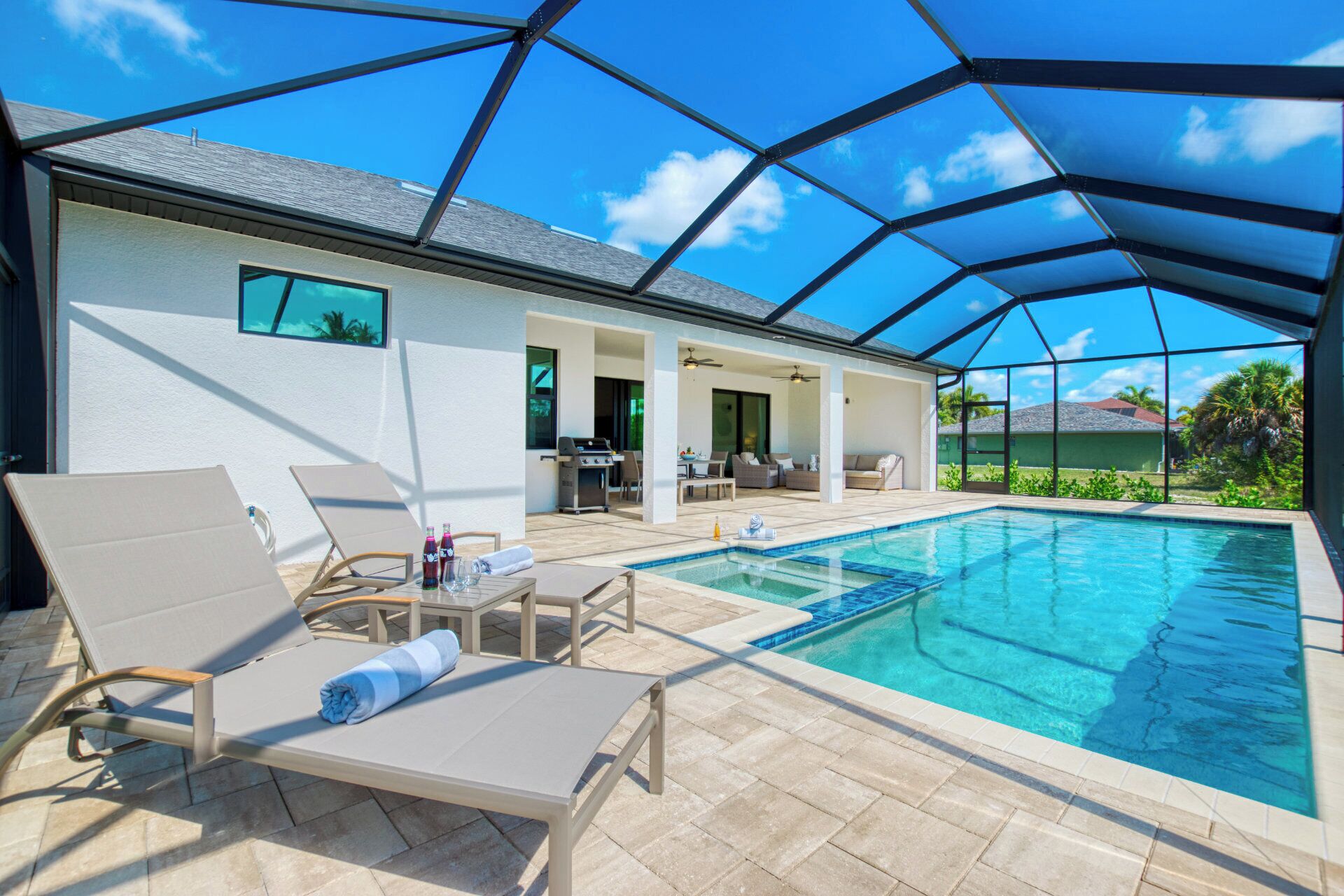 A covered outdoor swimming pool area with lounge chairs, a barbecue grill, and a patio with outdoor furniture.