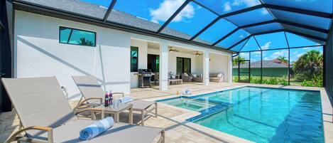 A covered outdoor swimming pool area with lounge chairs, a barbecue grill, and a patio with outdoor furniture.