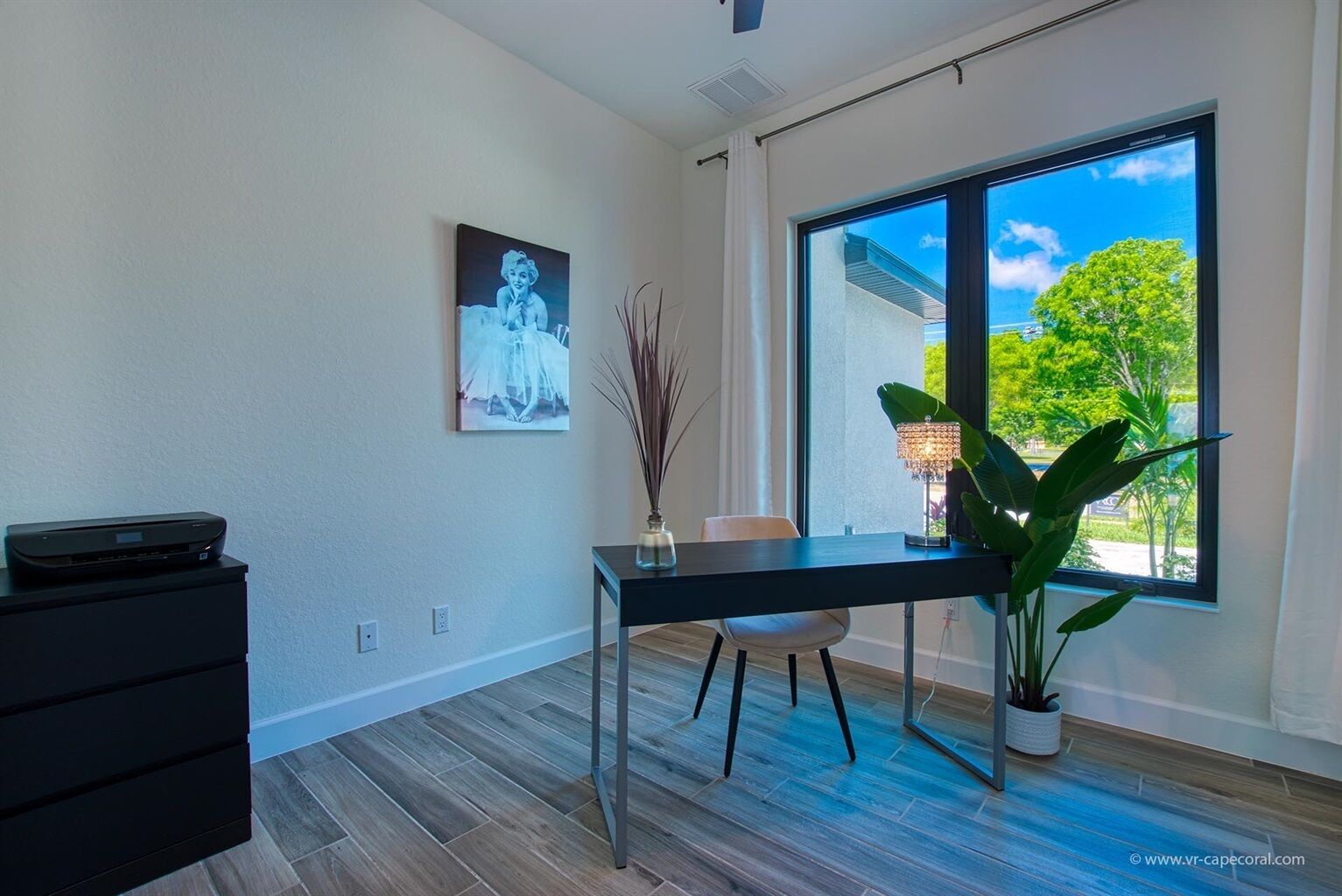 Quarto moderno com uma janela grande, uma escrivaninha, uma cadeira, um vaso de planta e um armário preto.