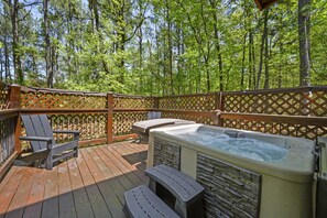 Eine Holzterrasse mit Whirlpool und Liegestühlen, umgeben von einem Holzzaun und Bäumen.